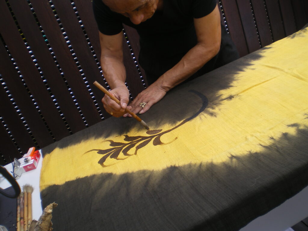 Cet artiste peint laa réserve avec de la cire fondue, il pulvérisera d'autres couleurs autour de la réserve, puis il éliminera la cire, à Kuching, Malaisie, au bout de mon âge